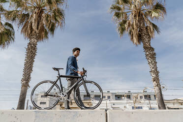 Mann mit Fahrrad, der an einem sonnigen Tag auf einer Stützmauer spazieren geht - AFVF08598