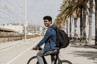 Lächelnder Mann mit Rucksack beim Fahrradfahren auf der Straße - AFVF08604