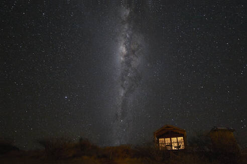 Milchstraße der südlichen Hemisphäre und eine kleine beleuchtete Hütte, Namibia, Afrika - RHPLF19498