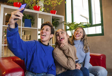 Lächelnde Studentinnen, die mit einem Notebook auf dem Sofa sitzen und in der Pause ein Selbstporträt mit dem Mobiltelefon aufnehmen - ADSF22565