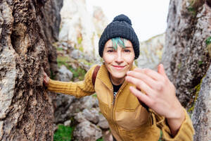 Positive junge Frau in Freizeitkleidung und Hut steht inmitten von Felsformationen und schaut zufrieden in die Kamera - ADSF22573