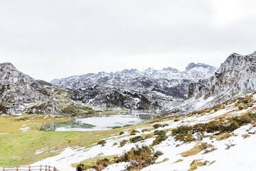 Spektakuläre Aussicht auf felsige, schneebedeckte Berge in der Nähe eines ruhigen Sees und ein weitläufiges, grasbewachsenes Tal in friedlicher Natur in Asturien - ADSF22584