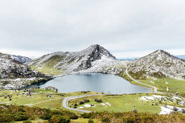 Spektakuläre Aussicht auf felsige, schneebedeckte Berge in der Nähe eines ruhigen Sees und ein weitläufiges, grasbewachsenes Tal in friedlicher Natur in Asturien - ADSF22585