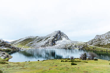 Spektakuläre Aussicht auf felsige, schneebedeckte Berge in der Nähe eines ruhigen Sees und ein weitläufiges, grasbewachsenes Tal in friedlicher Natur in Asturien - ADSF22586