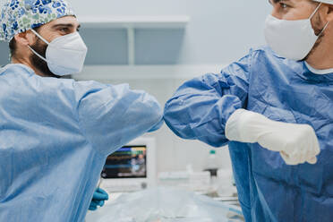 Anonyme männliche Tierärzte in Atemschutzmasken, die sich bei der Begrüßung vor einem chirurgischen Eingriff in der Klinik ansehen und sich dabei die Ellbogen stoßen - ADSF22636