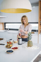 Cheerful woman blending fruits in kitchen at home - MPPF01628