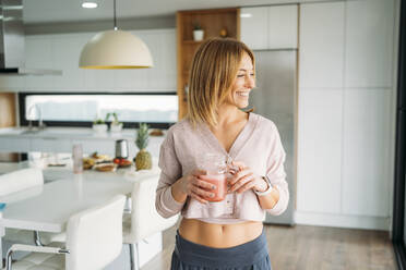 Caucasian woman with jar of juice looking away while standing in kitchen - MPPF01630