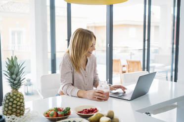 Smiling female freelancer working on laptop in kitchen at home - MPPF01631