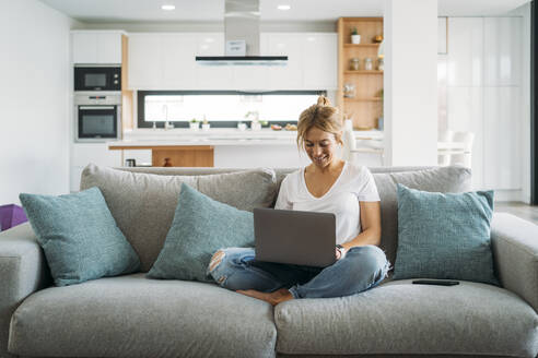 Berufstätige Frau, die zu Hause auf dem Sofa sitzend einen Laptop benutzt - MPPF01652