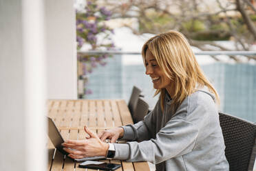 Lächelnde Berufstätige mit Laptop auf dem Balkon zu Hause - MPPF01655