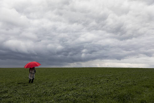 Frau mit rotem Regenschirm im Gras stehend bei stürmischem Wetter - FLLF00590