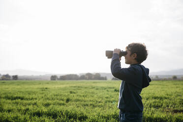 Junge schaut durch ein Fernglas auf ein landwirtschaftliches Feld an einem sonnigen Tag - JRFF05125