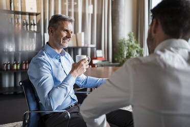 Älterer Geschäftsmann mit Kaffeetasse im Gespräch mit einem männlichen Kollegen am Arbeitsplatz - DIGF15127