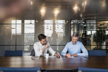Männlicher Unternehmer schreibt auf Papier, während er mit einem Kollegen im Sitzungssaal arbeitet - DIGF15129