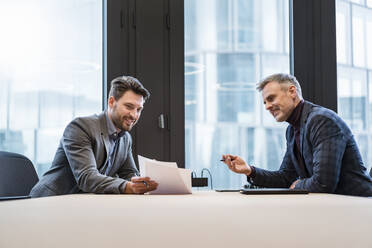 Smiling businessmen discussing over documents at table in office - DIGF15139