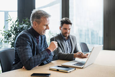 Lächelnde männliche Unternehmer, die über einen Laptop diskutieren, während sie im Büro arbeiten - DIGF15151