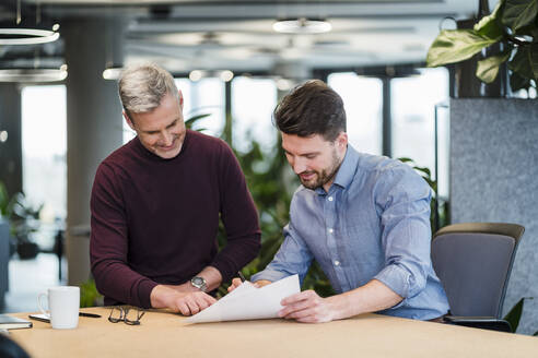 Geschäftsmann und männlicher Kollege diskutieren über Dokumente am Tisch im Büro - DIGF15157