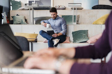 Mittlerer erwachsener Geschäftsmann mit Kaffeetasse bei der Arbeit an einem digitalen Tablet am Arbeitsplatz - DIGF15173