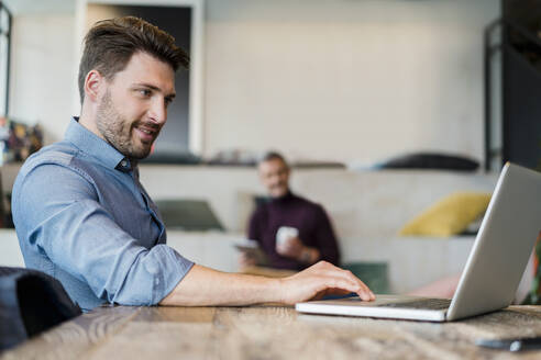Männlicher Berufstätiger mit Laptop bei der Arbeit im Büro - DIGF15174