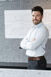 Male entrepreneur with arms crossed standing in office - DIGF15187