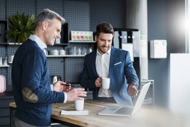 Business people discussing over laptop while having coffee in office cafe - DIGF15190