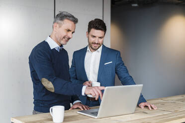 Männliche Unternehmer trinken Kaffee, während sie am Arbeitsplatz über einen Laptop sprechen - DIGF15193