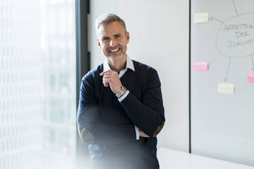 Smiling mature businessman standing by whiteboard in office - DIGF15206