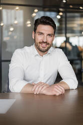 Smiling businessman leaning on table at office - DIGF15223