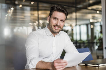 Smiling male professional with paper document at work place - DIGF15224