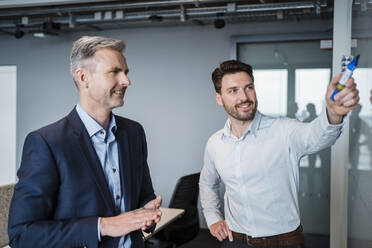 Smiling business people discussing over whiteboard in meeting at work place - DIGF15258