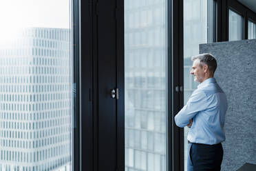 Mature male professional looking through window in office - DIGF15275