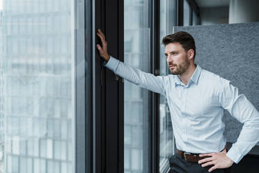 Businessman with hand on hip day dreaming at office - DIGF15276