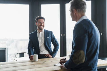 Lächelnder Geschäftsmann, der Kaffee trinkt und einen männlichen Kollegen im Büro betrachtet - DIGF15281
