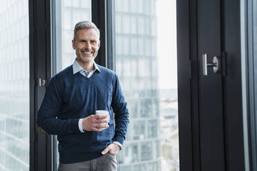 Männlicher Fachmann mit Kaffeetasse am Fenster im Büro stehend - DIGF15284