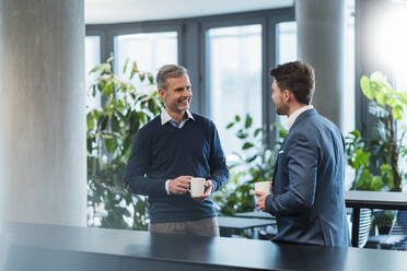 Lächelnde Geschäftsleute, die eine Kaffeetasse halten, während sie sich in einem Café am Arbeitsplatz unterhalten - DIGF15293