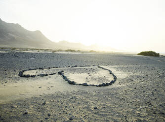 Spanien, Kanarische Inseln, Fuerteventura, Herzform aus Steinen am Sandstrand Playa de Cofete bei Sonnenuntergang - CVF01703
