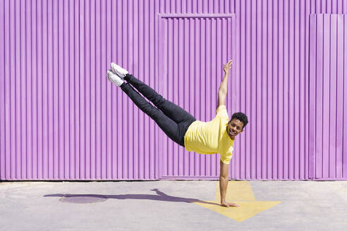 Smiling man balancing on handstand in front of cabin - JSMF02109