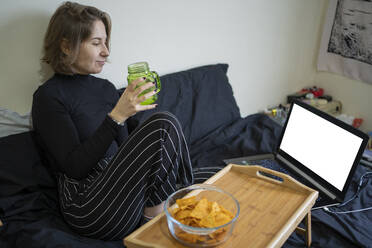 Young woman having juice while looking at laptop at home - FBAF01793