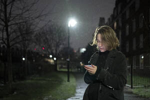 Frau benutzt Mobiltelefon, während sie nachts auf der Straße steht - FBAF01801