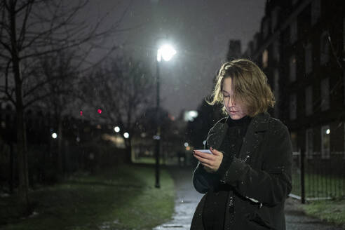 Woman using mobile phone while standing on road at night - FBAF01801