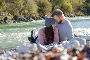 Young couple lying on pebbles at lakeshore during sunny day - LBF03500