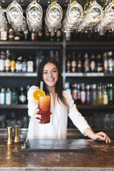 Lächelnde weibliche Barkeeperin gibt ein Glas Cocktail am Tresen - JAQF00475