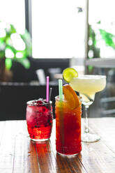 Garnished glasses of cocktails on table at bar - JAQF00487