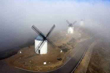 Spain, Province of Toledo, Consuegra, Aerial view of country road stretching past historical windmills during foggy weather - DSGF02404