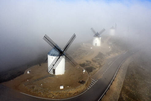 Spain, Province of Toledo, Consuegra, Aerial view of country road stretching past historical windmills during foggy weather - DSGF02404