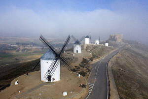 Spain, Province of Toledo, Consuegra, Aerial view of country road stretching past historical windmills - DSGF02406