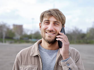 Lächelnder gutaussehender Mann, der mit einem Mobiltelefon spricht - FMKF07075