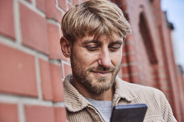 Man with blond hair using smart phone by building - FMKF07089