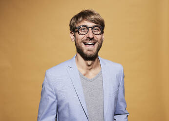 Man wearing eyeglasses laughing in front of yellow wall - FMKF07106