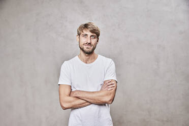 Confident man with arms crossed standing in front of wall - FMKF07116